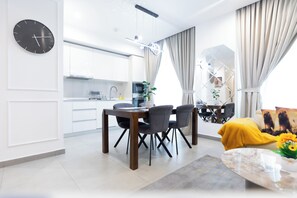 Una cocina moderna con gabinetes blancos, una mesa de comedor con sillas y una sala de estar con sofá y mesa de centro.