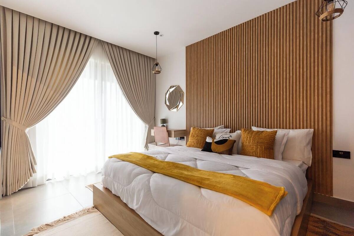 A modern bedroom with a large bed, a wooden panel wall, and a large window with curtains.