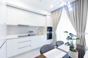 A modern kitchen with white cabinets, a Bosch dishwasher, and an oven. There is a dining area with a table and chairs, and a plant on the table.