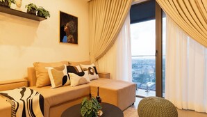 A modern living room with a beige sofa, a black coffee table, and a view of the city through large windows. - NOVA-BlueWaters Property Management (Accra)