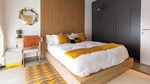 A modern bedroom with a large bed, a wooden headboard, a dark wardrobe, and a geometric-patterned rug. - NOVA-BlueWaters Property Management (Accra)