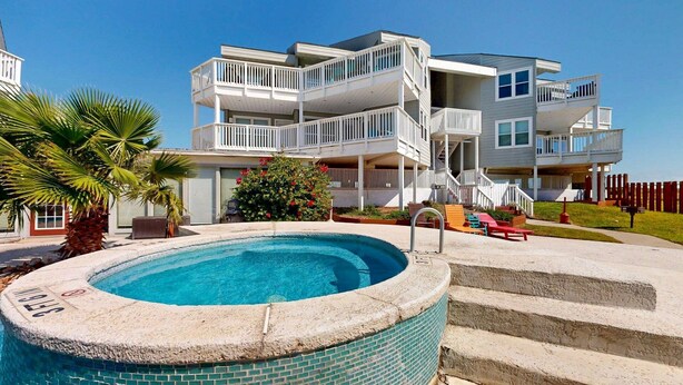 A multi-story residential building with a swimming pool, outdoor seating, and a staircase leading to the upper levels. - Shared Pool, Hot Tub, Pet Friendly (Port Aransas)