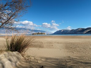 Une plage avec un ciel dégagé, des montagnes en arrière-plan et une végétation clairsemée.