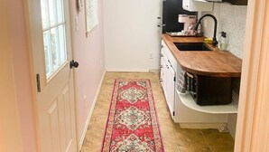 Una cocina compacta con encimera de madera, un fregadero y un refrigerador negro. Una alfombra roja con estampado cubre el suelo, y hay un cuadro en la pared.