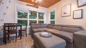 Ein modernes Wohnzimmer mit einem Ecksofa, einer Holzlade und einem Essbereich mit einem dunklen Holztisch und Stühlen.