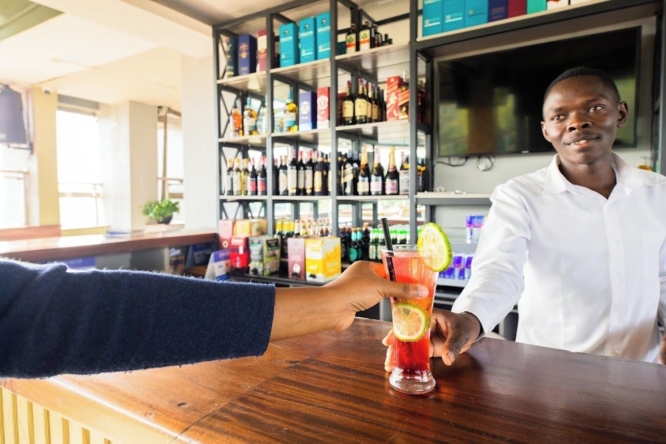 A bar setting with a person holding a drink and another person behind the bar.
