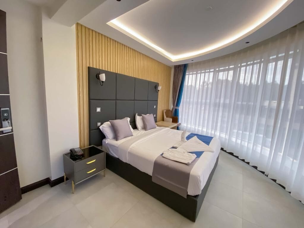 Una habitación de hotel moderna con una cama grande, una mesita de noche con teléfono y un cabecero con iluminación integrada.