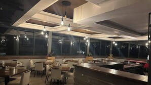 A modern restaurant interior with high ceilings, pendant lighting, and large windows. Tables and chairs are arranged for dining. - Zuri Place Hotel (Oyugis)