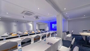 A conference room with rows of tables and chairs, a projector screen, and a whiteboard. - Zuri Place Hotel (Oyugis)