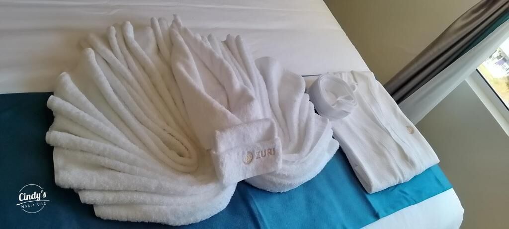 Un juego de toallas blancas dobladas ordenadamente sobre una cama con una colcha azul.