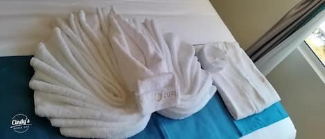 A neatly folded set of white towels on a bed with a blue bedspread.