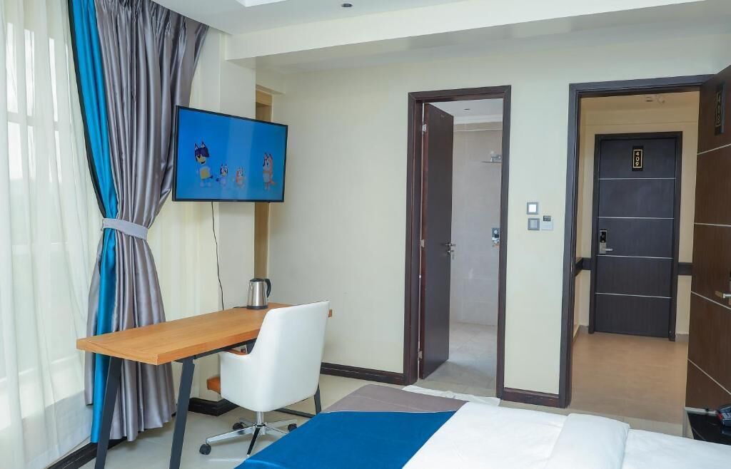 Une chambre d’hôtel comprenant un lit, un bureau, une chaise, une télévision et une porte donnant sur une autre pièce.