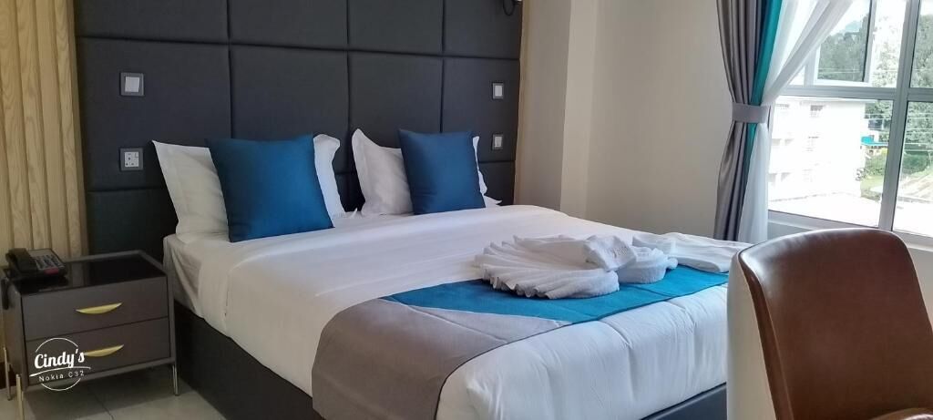A hotel room with a bed, a nightstand, a chair, and a window with curtains.