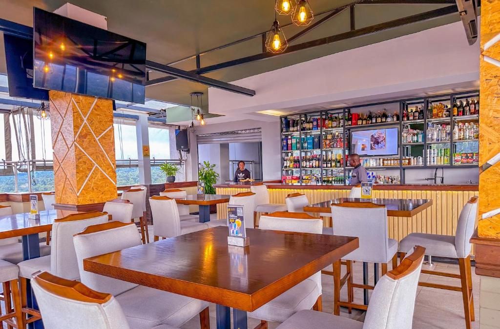 Un'area bar moderna con diverse bottiglie di liquore, uno schermo televisivo e una zona salotto con tavoli e sedie.