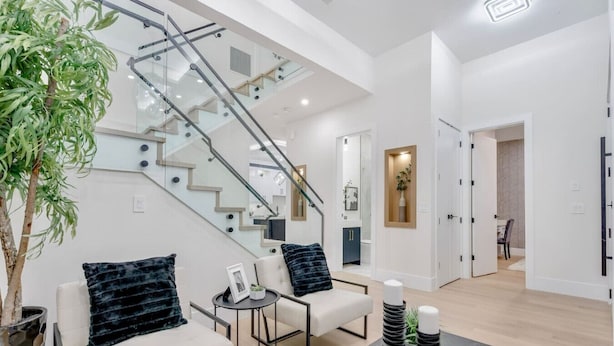 Un salon moderne avec un escalier, un ensemble de canapés, une table basse et une plante en pot.