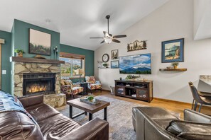 A living room with a stone fireplace, leather sofas, a coffee table, and a ceiling fan. - Modern Flagstaff Escape 2BR/2BA, Trails & Views (Flagstaff)
