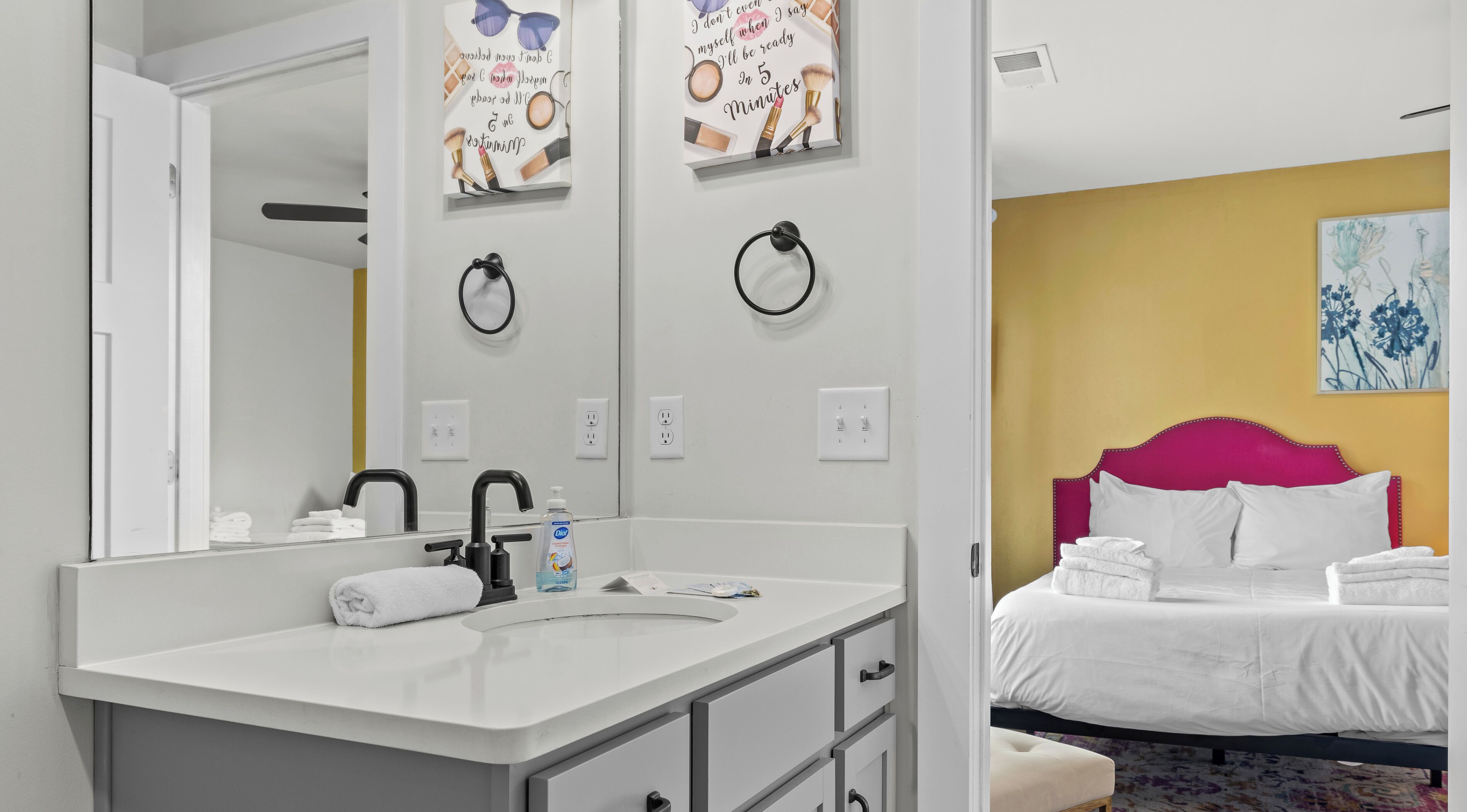 Ett modernt hotellrum med en vit sminkbord, en säng med en rosa sänggavel och en stor spegel.