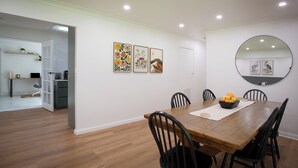 A dining area with a wooden table, black chairs, and a bowl of fruit on the table. There are three framed artworks on the wall and a round mirror above the table. - Highland Heart Cottage, Newly Renovated, Spacious & Family Friendly (Bowral)
