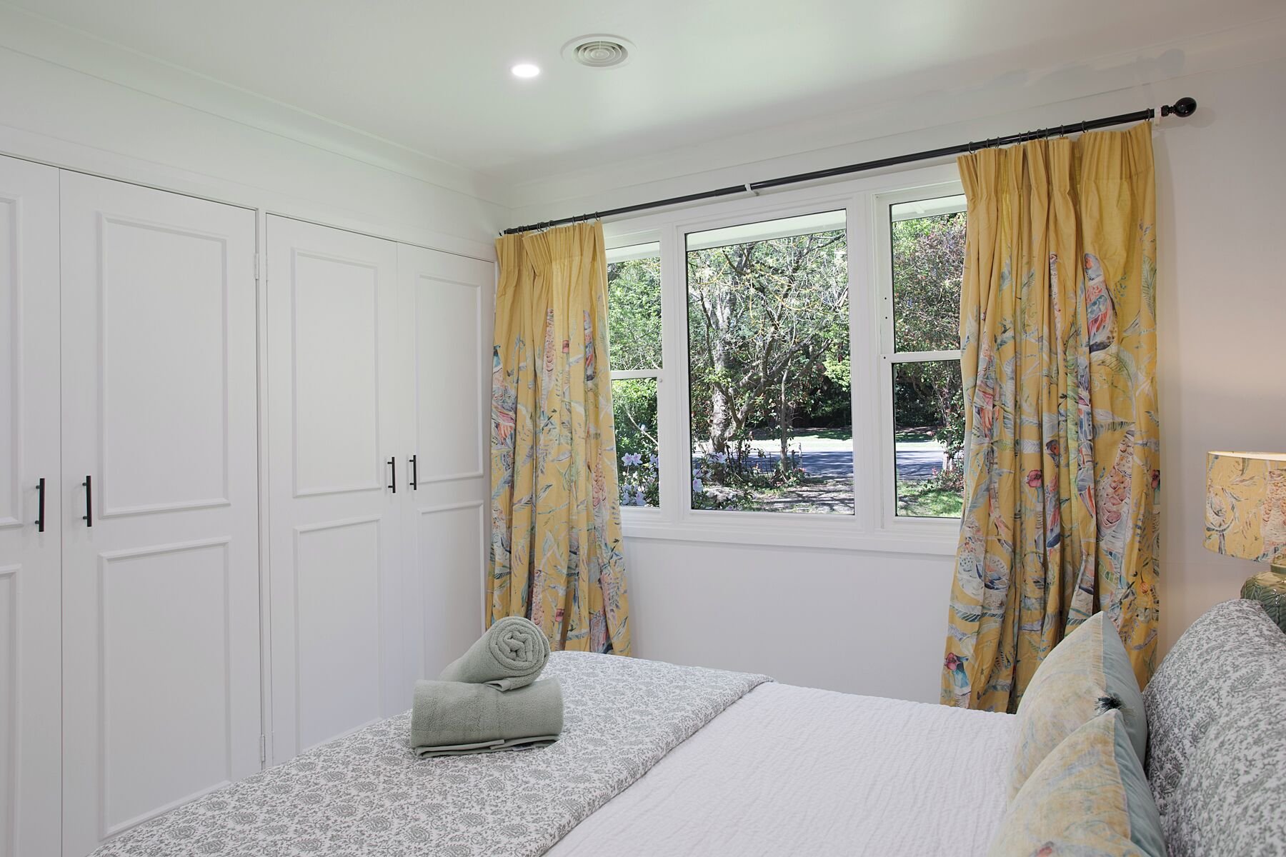 A bedroom with a bed, a window with curtains, a wardrobe, and a lamp.
