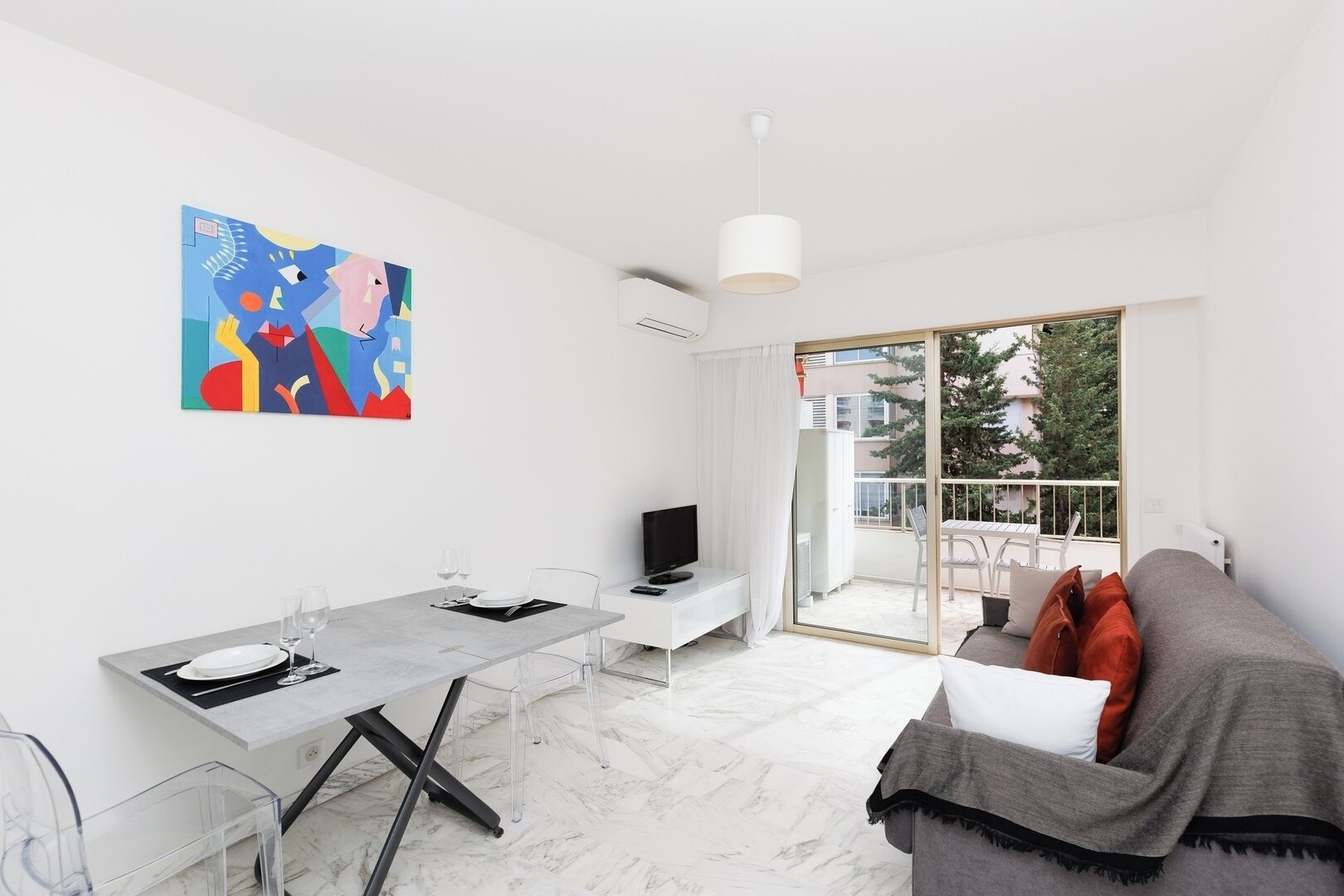 Un appartement moderne comprenant un coin repas, un canapé, une télévision et un balcon offrant une vue sur les arbres et les immeubles.
