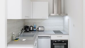 Una cocina moderna con armarios blancos, una campana extractora de acero inoxidable, una cafetera, un tostador y un lavavajillas.