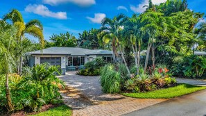 Une maison avec une allée pavée, entourée d’une végétation tropicale luxuriante et de palmiers.