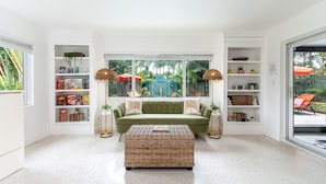 Un salon avec un canapé vert, un pouf en osier et des étagères remplies de livres et d’objets décoratifs.
