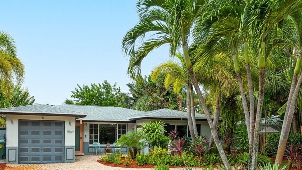 Une maison à deux étages avec un garage, entourée d’une végétation tropicale luxuriante.