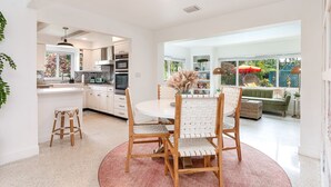 Une cuisine moderne avec des meubles blancs, un îlot central et un coin repas comprenant une table ronde et des chaises.