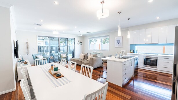 A modern kitchen with white cabinets, a central island, and a dining area with a white table and chairs. - The Lake House—Spacious Group Haven by the Bay (Victor Harbor)
