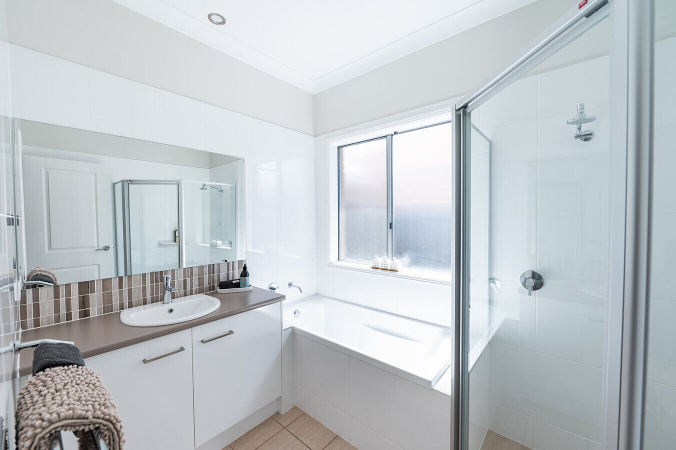 A modern bathroom with a glass shower enclosure, a large window, and a white sink.