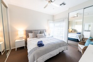 A modern bedroom with a large bed, a nightstand, a mirror, and a ceiling fan. - The Lake House—Spacious Group Haven by the Bay (Victor Harbor)