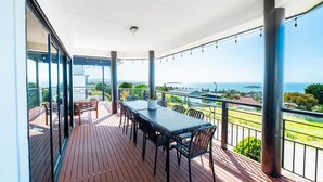 A covered outdoor balcony with a table and chairs, overlooking a scenic view of the sea and landscape. - BaeView: Panoramic Group Stay Above Encounter Bay (Encounter Bay)