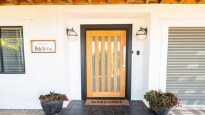 A house entrance with a wooden door, a welcome mat, and two potted plants. - BaeView: Panoramic Group Stay Above Encounter Bay (Encounter Bay)