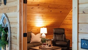 A cozy log cabin interior with a wooden ceiling, a sofa, a chair, and a table with a lamp. - Lake Bemidji retreat- modern, cozy cabin spacious enough for family and friends. (Bemidji)