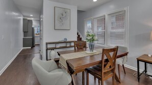 Un comedor con una mesa de madera, sillas y un florero. Se ve una escalera que conduce a otra habitación.