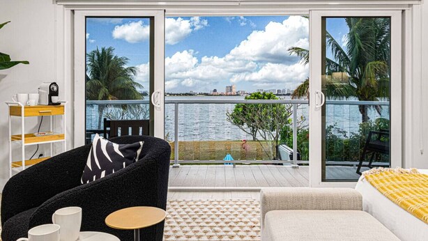 Ein modernes Zimmer mit Balkon und Blick auf ein Gewässer, ausgestattet mit einer Couch, einem kleinen Tisch und einer Kaffeestation.