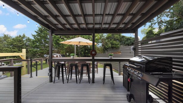 Eine überdachte Terrasse im Freien mit Grill, Barhocker und Sonnenschirm.