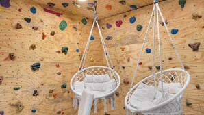 Eine Kletterwand mit bunten Griffen und zwei weißen Hängestühlen.