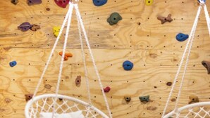 Ein Zimmer mit zwei weißen Hängesesseln und einer Kletterwand aus Holz.