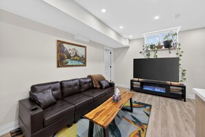Een moderne woonkamer met een bruine leren bank, een houten salontafel, een flatscreen televisie en een schilderij aan de muur.