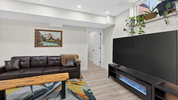Una sala de estar moderna con un sofá de cuero marrón oscuro, una mesa de centro de madera, un televisor de pantalla plana y una chimenea.