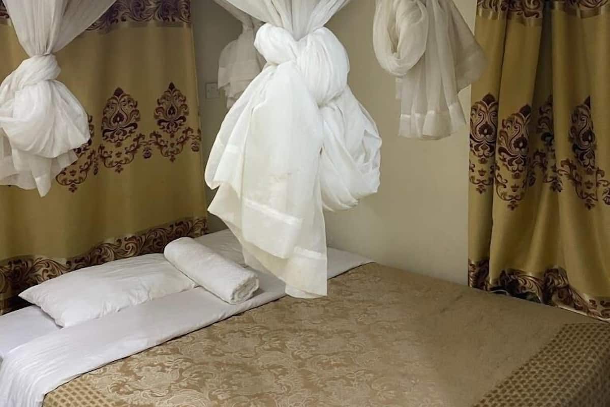 A room with a bed, white curtains, and patterned curtains.