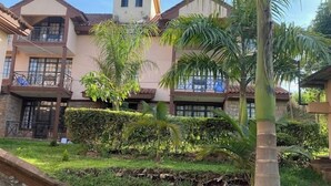 Una casa de dos pisos con balcón, rodeada de césped cuidado y palmeras.
