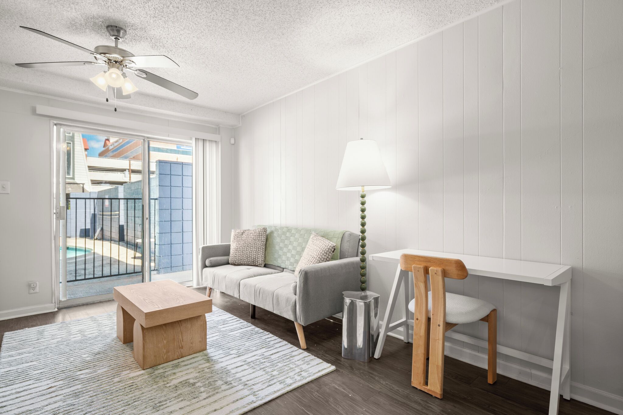 A modern living room with a grey sofa, a wooden coffee table, a white desk, and a standing lamp.