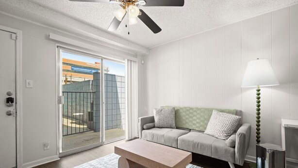 A modern living room with a sliding glass door leading to a balcony, a grey sofa, a wooden coffee table, and a floor lamp. - Cozy Studio Walk to UT & Moody 7 Min to ACL (Austin)