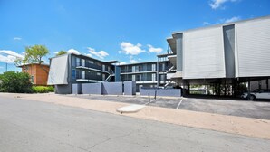 A modern building with multiple floors, large windows, and a parking area in front. - Cozy Studio Walk to UT & Moody 7 Min to ACL (Austin)