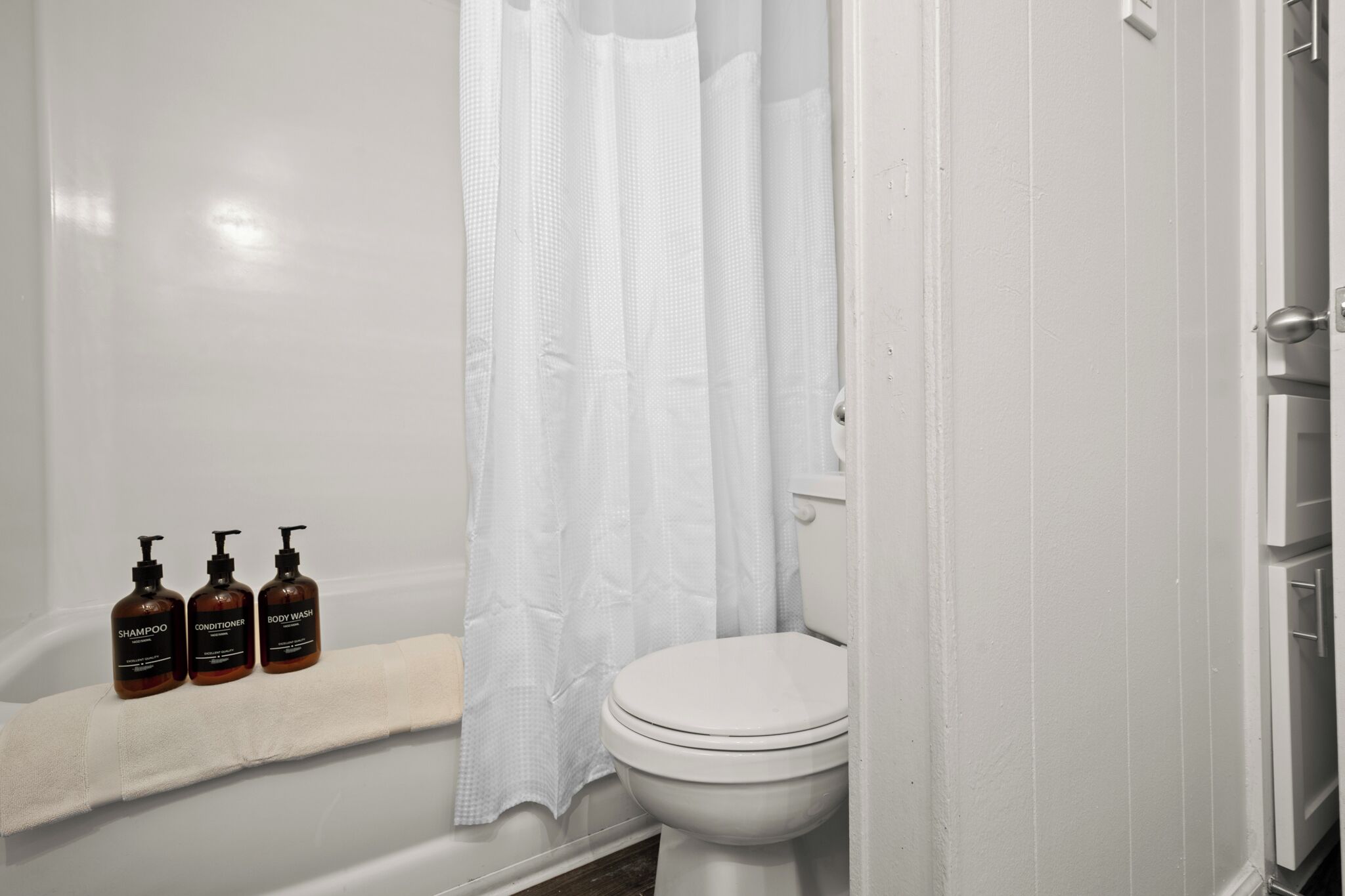A bathroom with a bathtub, toilet, and a shelf with three bottles of toiletries.