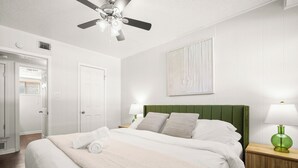 A neatly arranged bedroom with a bed, a green headboard, two bedside lamps, a ceiling fan, and a painting on the wall. - Cozy Studio Walk to UT & Moody 7 Min to ACL (Austin)