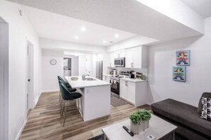 A modern kitchen with white cabinets, a central island, and a dining area with bar stools. - 2BR Guest Suite - Elegant, Private & Well-Equipped (Calgary)